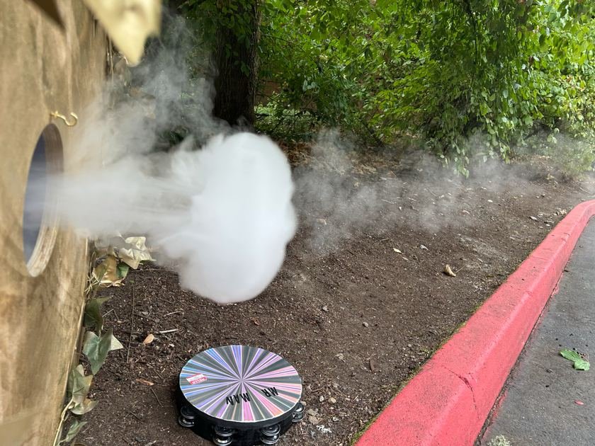 Ground-level view of fog discharging from the orifice toward the curb and treeline
